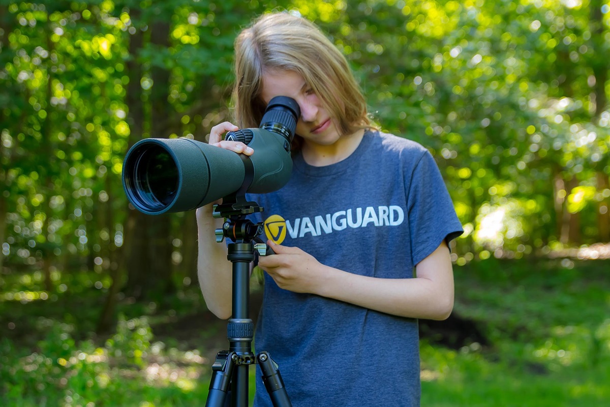 Ребёнок наблюдает в подзорную трубу на штативе Vanguard Vesta Go 264AV12 и держит рукоятку головки